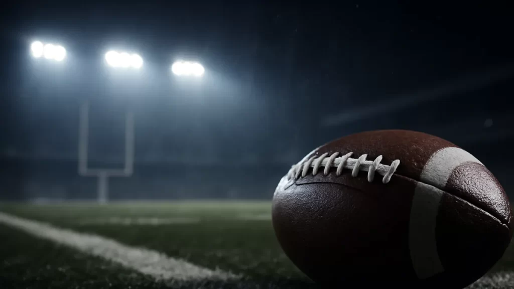 Ravens exploit overtime rules to beat Falcons 30-23 in dramatic finish Close-up football on wet turf under stadium floodlights, blurred empty stands.